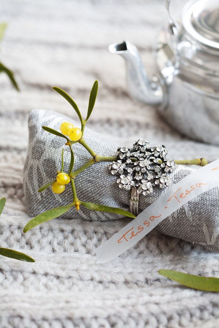 A linen napkin decorated with a sprig of mistletoe and a ring with a transparent strip of paper as a name tag