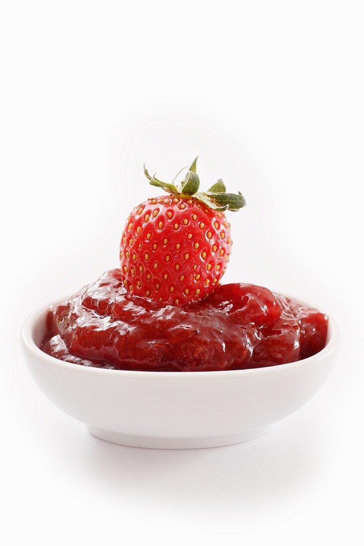A bowl of strawberry jam topped with a fresh strawberry