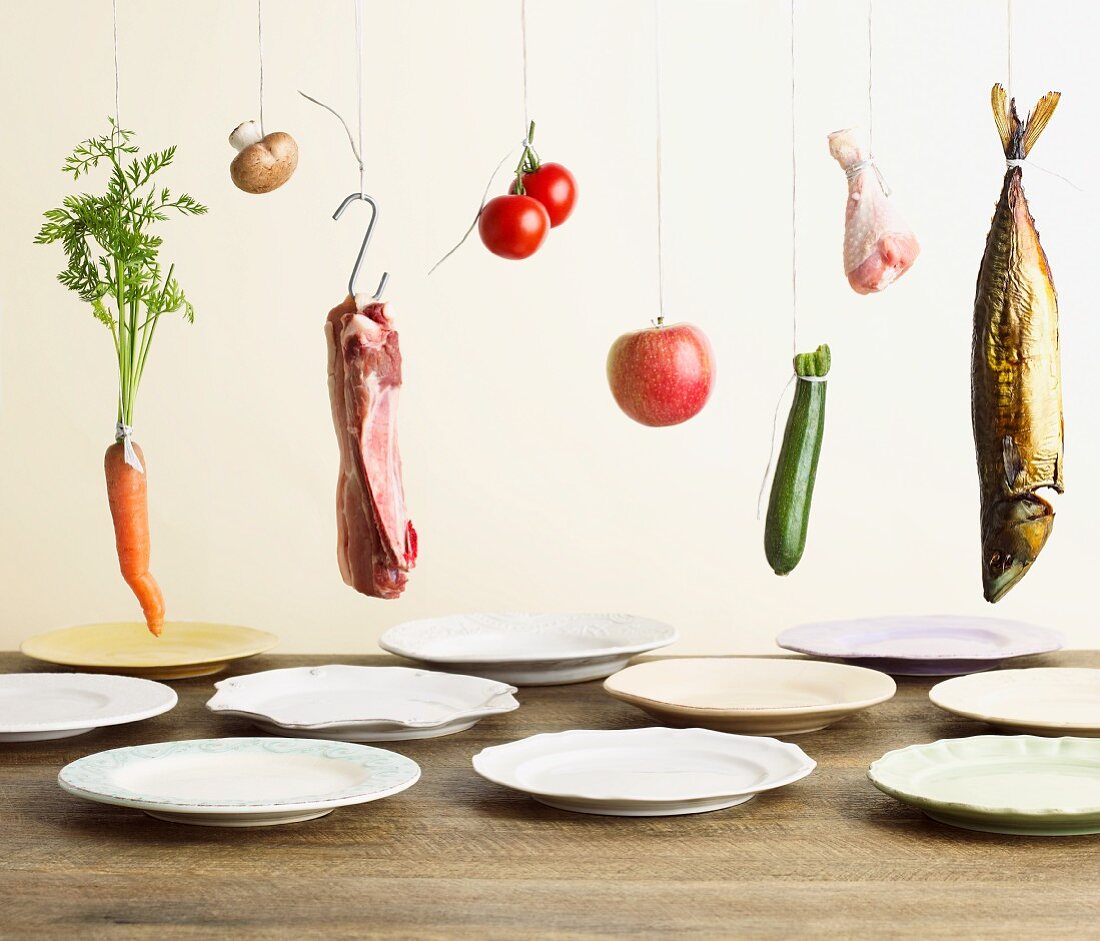 Vegetables, meat, poultry and fish hanging above plates