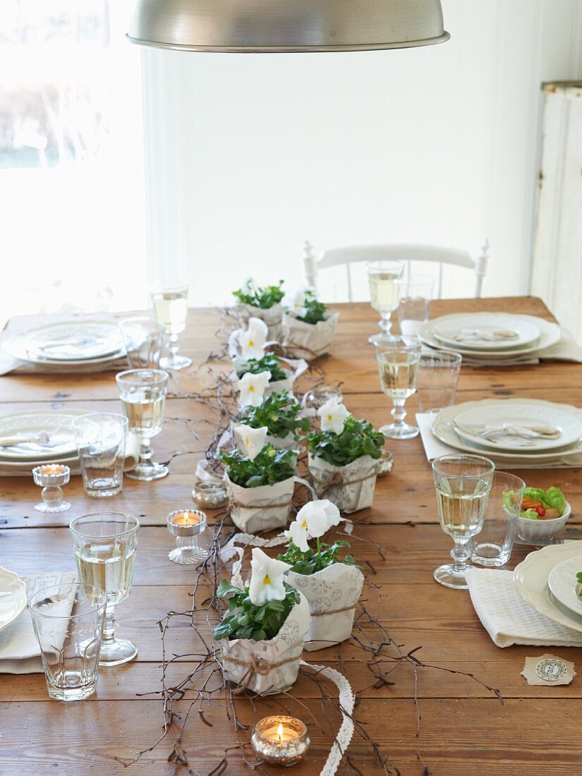 Gedeckter Holztisch mit weissen Stiefmütterchen, Teelichtern und Weißwein