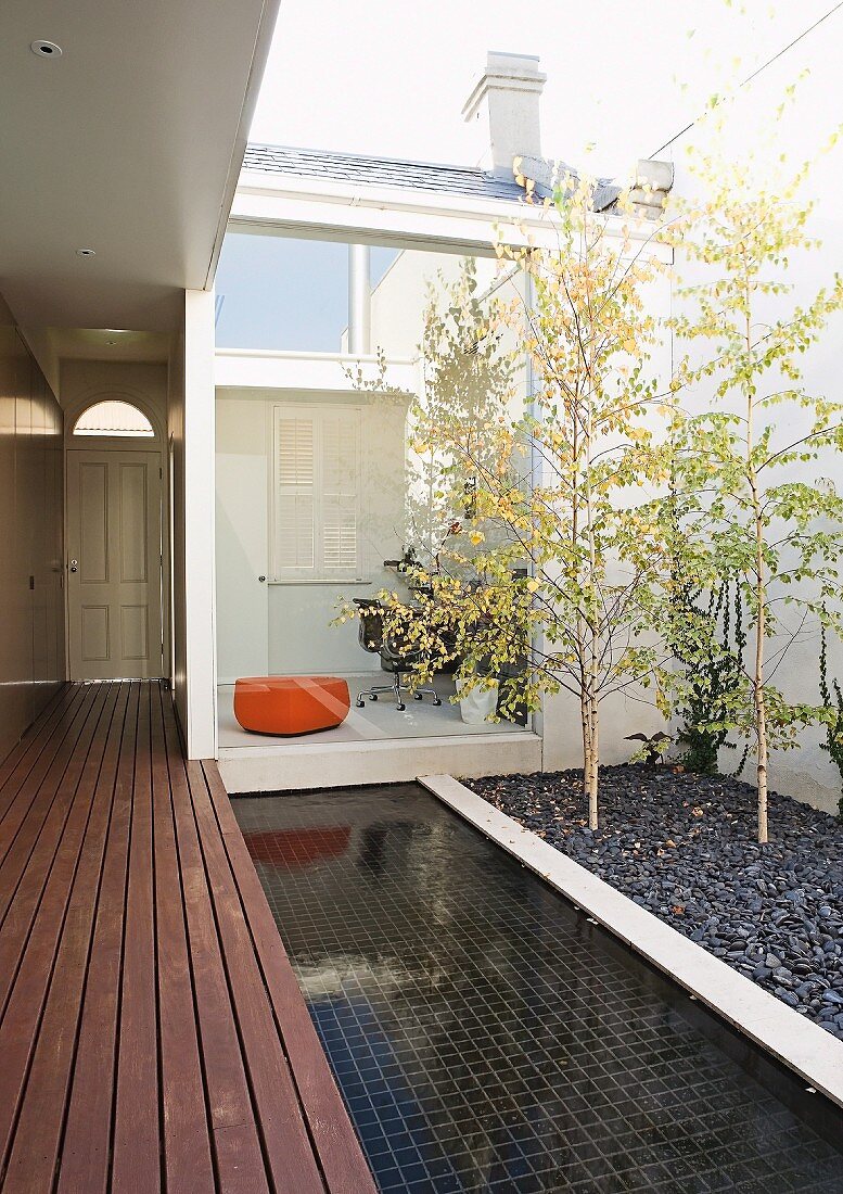 Entrance to courtyard of house with separate home office; purist design with wooden platform, pool and birches in gravel bed