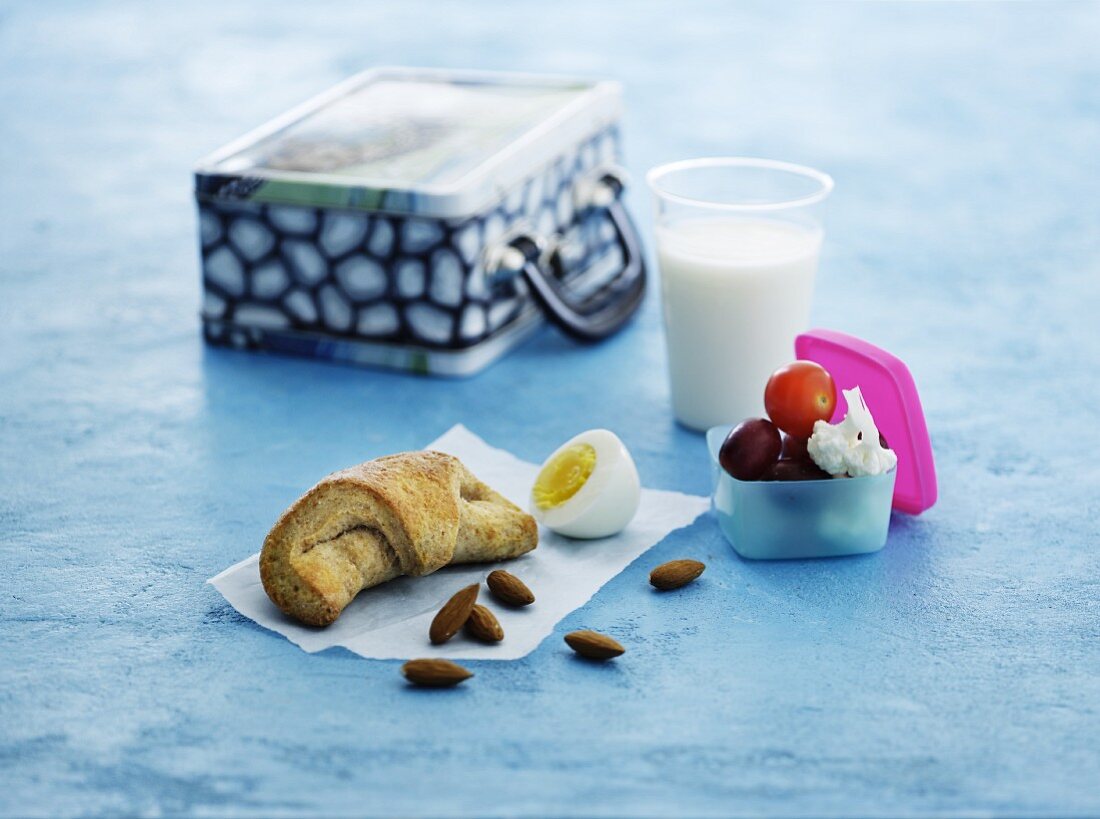 A croissant, a hard-boiled eggs, almonds, fruit, vegetables and milk for lunch