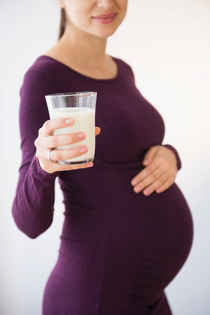 A pregnant woman in a purple dress holding a glass of milk