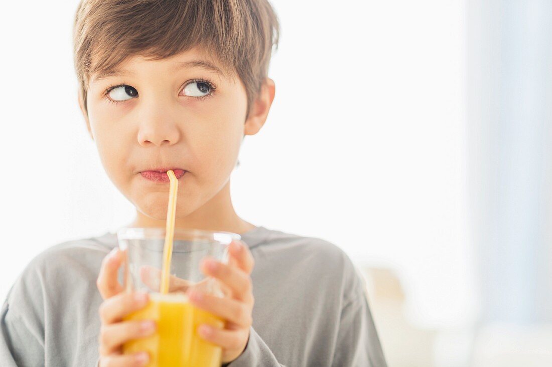 Kleiner Junge trinkt Orangensaft aus Glas mit Strohhalm