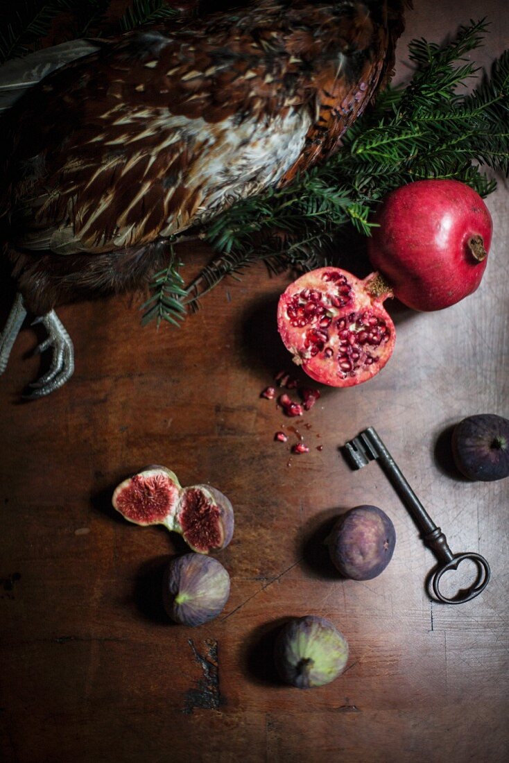 An arrangement featuring pheasant, pomegranates and figs