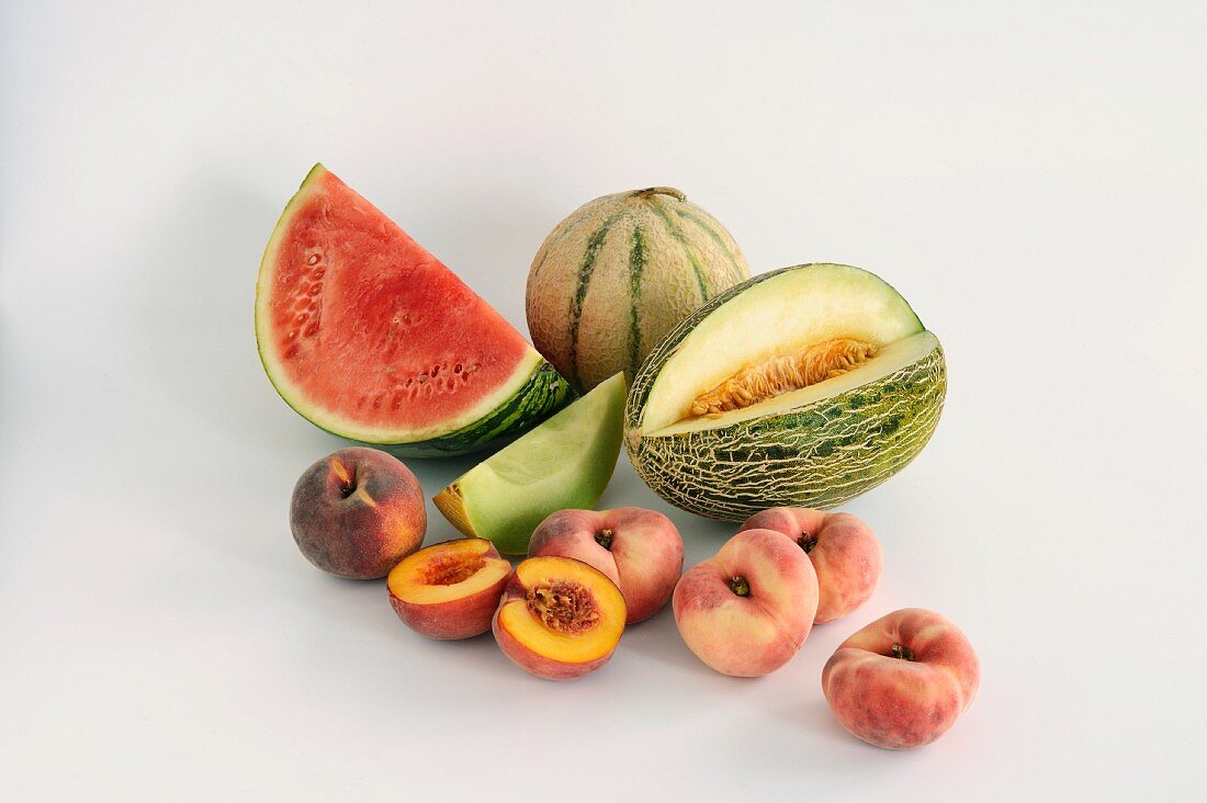 Various different melons and peaches against a white background