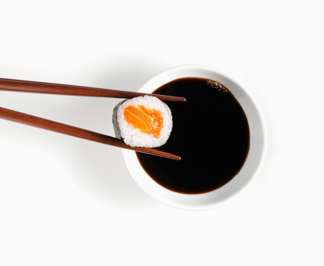 Maki-Sushi auf Essstäbchen über einem Schälchen Sojasauce
