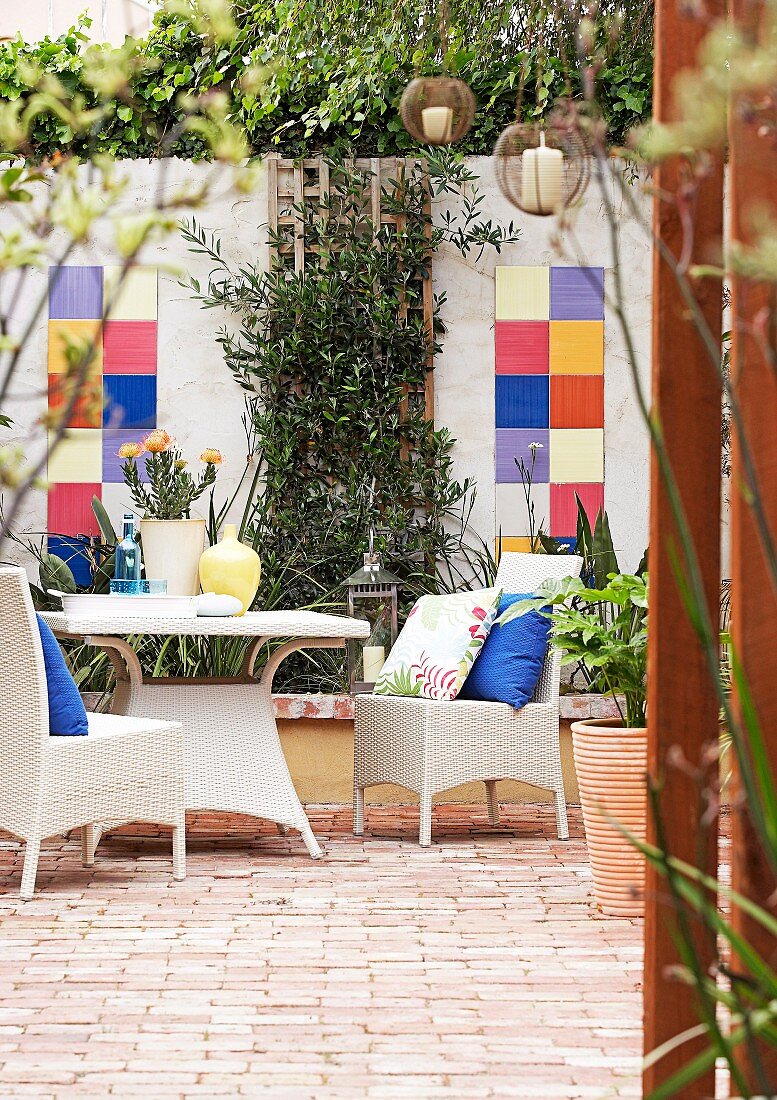 weiße Rattan Outdoormöbel auf Terrasse mit Terrakottaboden und bunte Fliesen an Mauer des Innenhofes