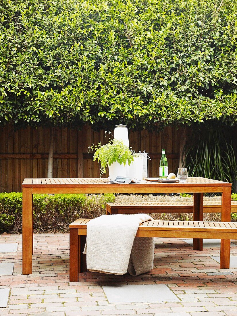 Dining area with wooden table and matching benches in brick-paved, planted courtyard