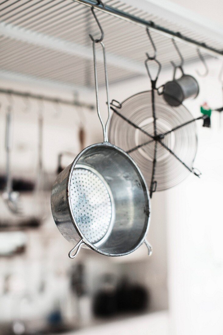 Retro metal colander and kitchen utensils hanging from rod below ceiling