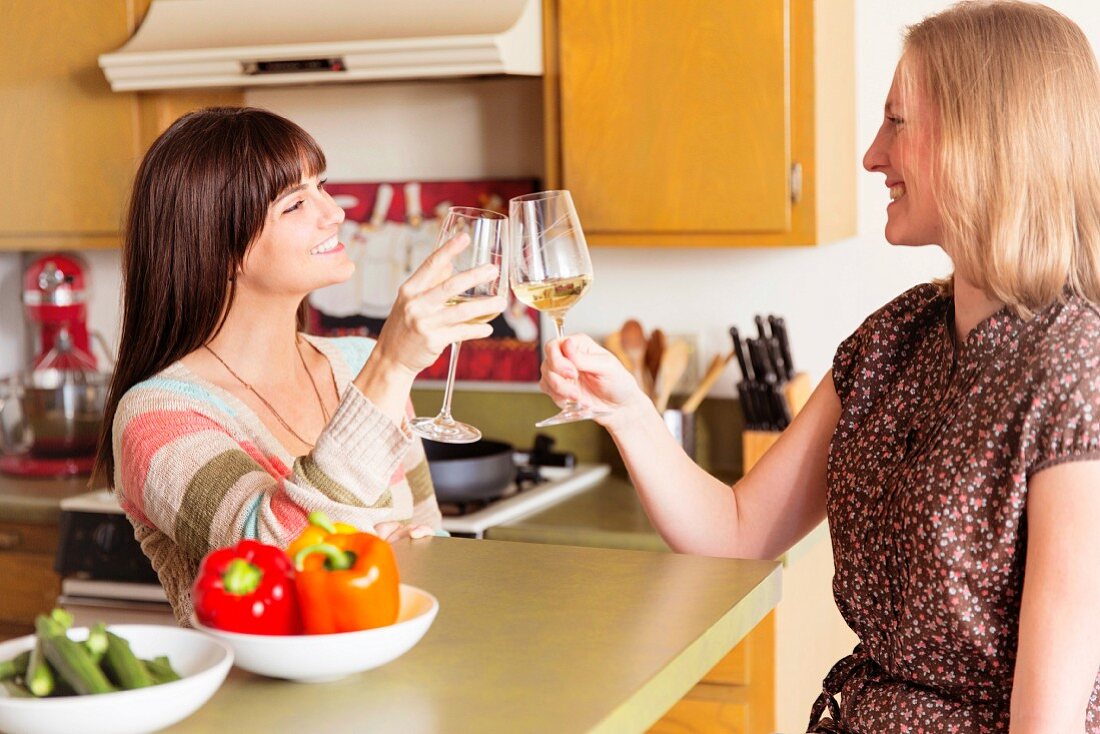 Two women raising a toast with wine glasses in kitchen