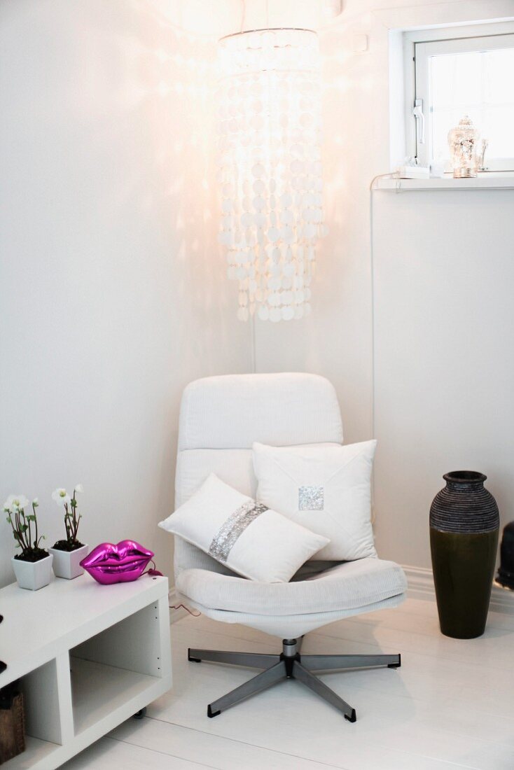 Scatter cushions with glittery print on swivel easy chair below magnificent capiz shell chandelier flanked by black floor case and purple lip-shaped ornament