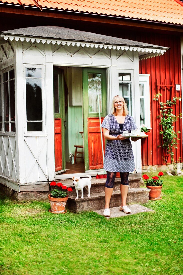 Smiling woman holding tray outside porch of Swedish wooden house