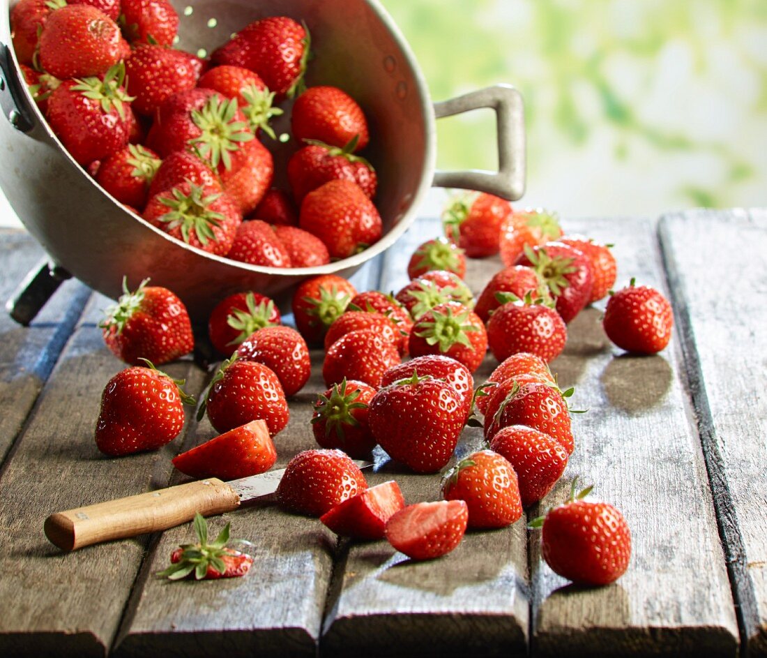 Frische Erdbeeren im Fussseiher und auf Holztisch, teilweise geschnitten