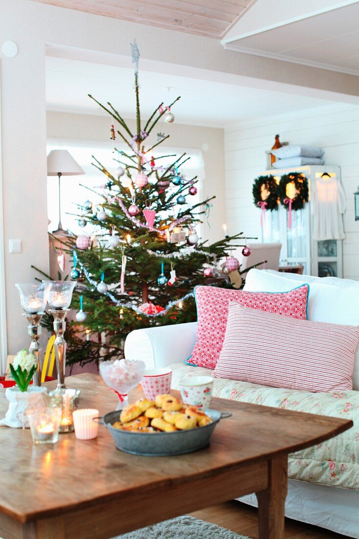 Scatter cushions on white sofa, rustic wooden coffee table and decorated Christmas tree in rustic living room