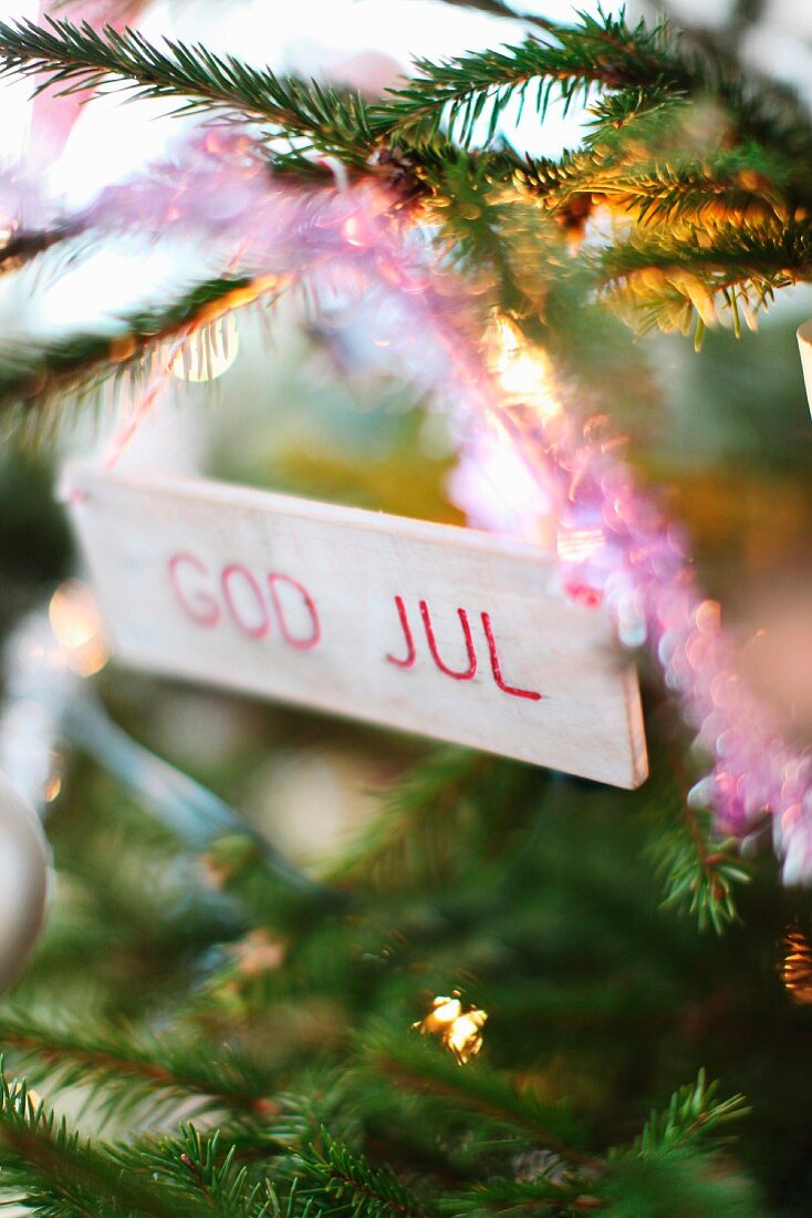 Small wooden sign with Christmas greetings hanging on fir tree