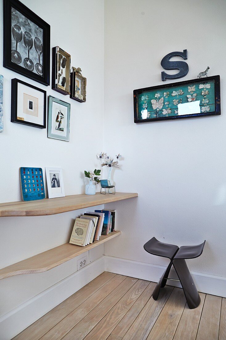 Dark wood Butterfly Stool by Sori Yanagi in corner next to books and ornaments on wooden, wall-mounted shelves below framed pictures