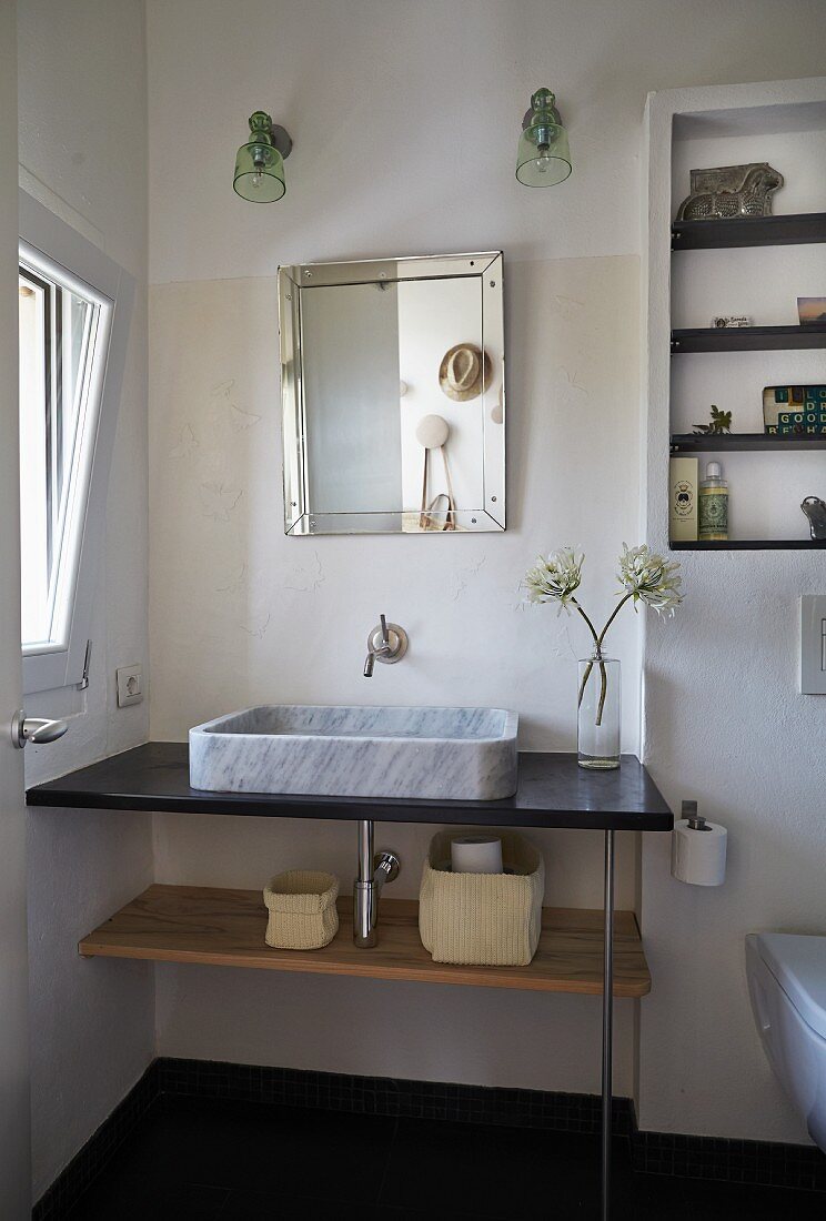 Modern washstand with marble countertop basin below mirror and two sconce lamps in corner of bathroom