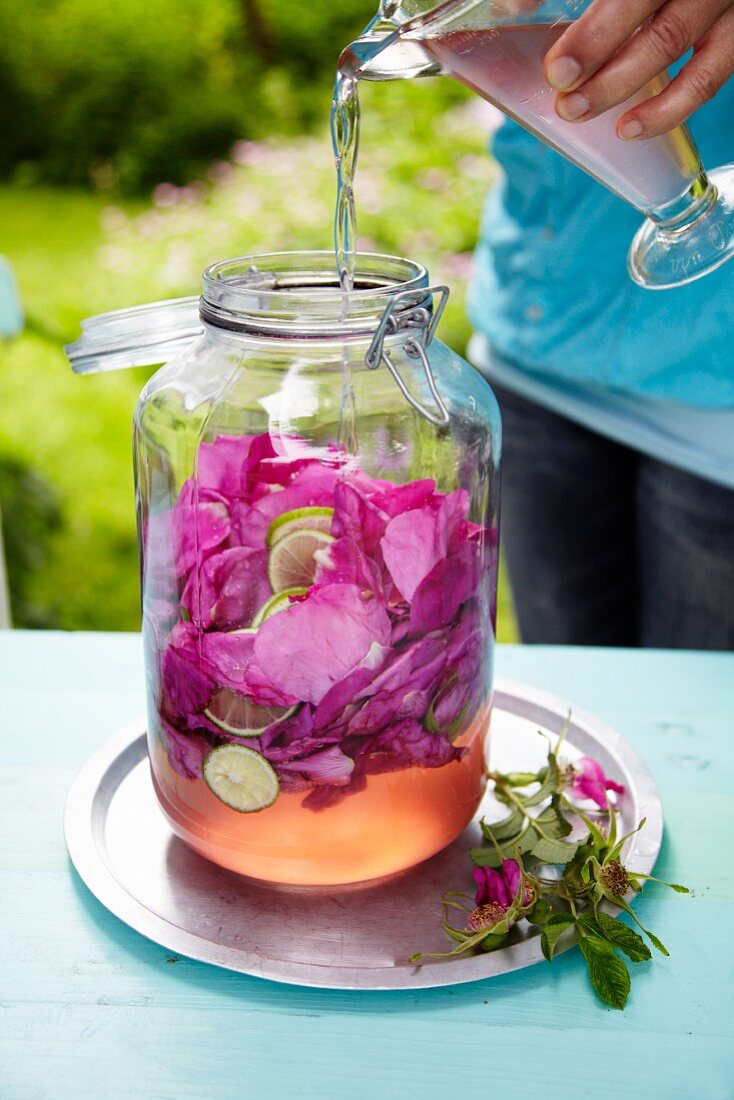 Water being poured over wild rose petals in a glass jar