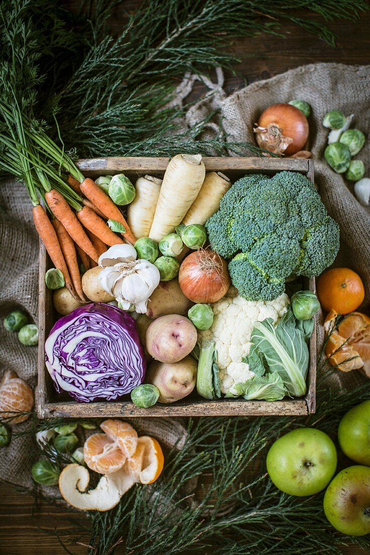 A crate of vegetables with apples and clementines