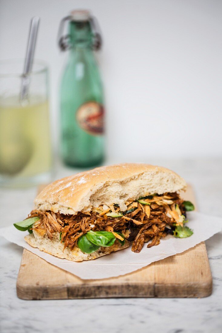 A pulled pork sandwich with basil on a chopping board