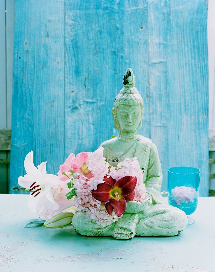 Buddha-Figur mit Stockrosen und Lilien