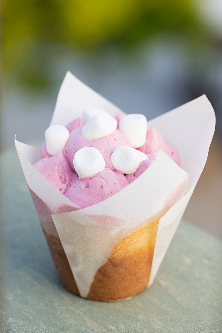 A vanilla cupcake decorated with raspberry cream and mini marshmallows