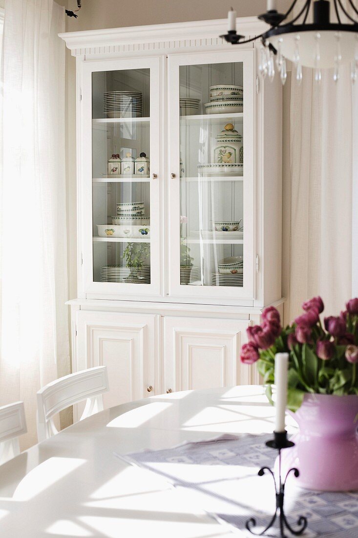 Candlestick and bouquet of tulips on dining table; country-house-style, glass-fronted dresser painted white in background