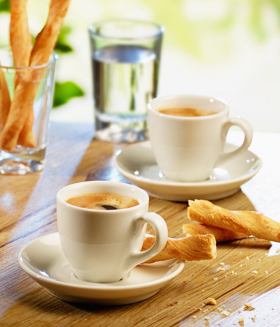 Zwei Tassen Espresso, Salzgebäck und Wasserglas auf Gartentisch