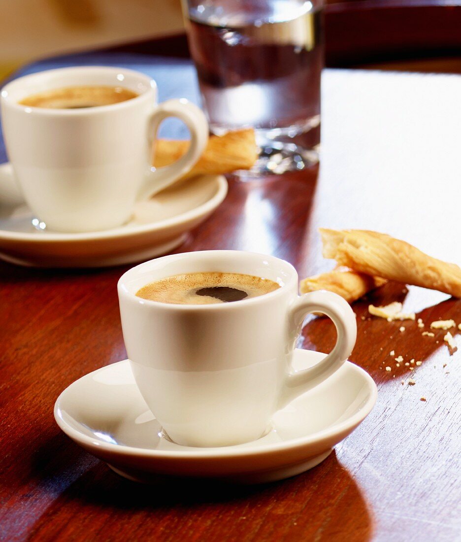 Drei Tassen Espresso, Salzgebäck und Kaffeebohnen auf Tisch