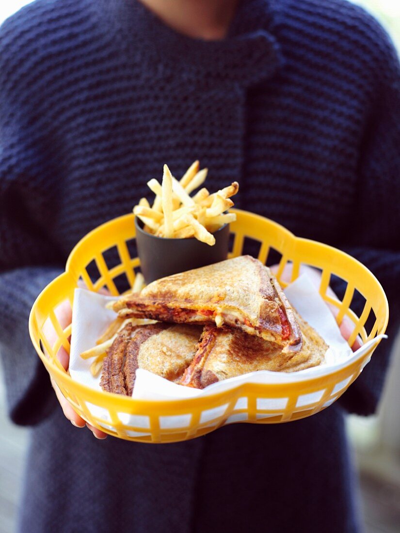 Frau hält Plastikkorb mit Schinken-Käse-Toasts und Pommes frites