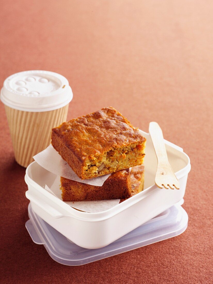 Möhrenkuchen in Lunchbox neben Kaffeebecher