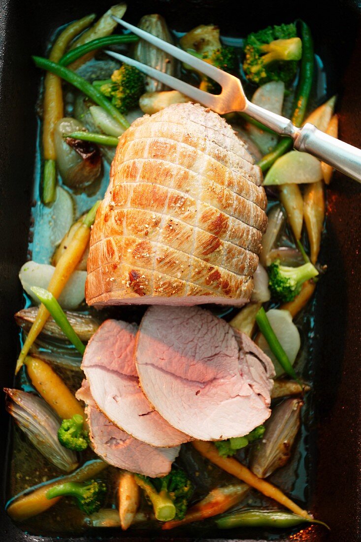 Roasted pork roulade on a bed of vegetables in a roasting tin with three slices cut