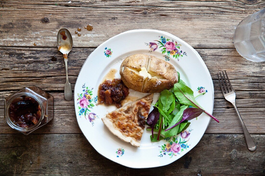 A slice of onion tart with baked potato, salad and apple and courgette chutney