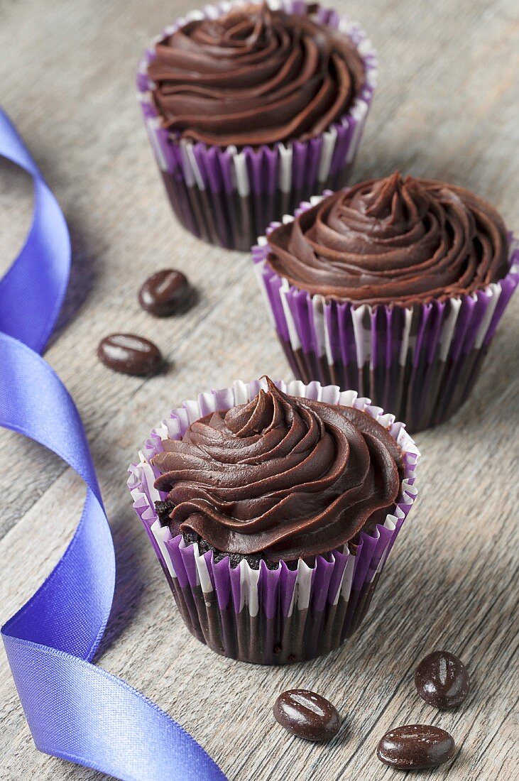Three chocolate ganache cupcakes with chocolate beans and a ribbon