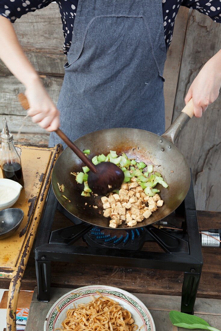 Wide rice noodles with tofu being fried in a wok