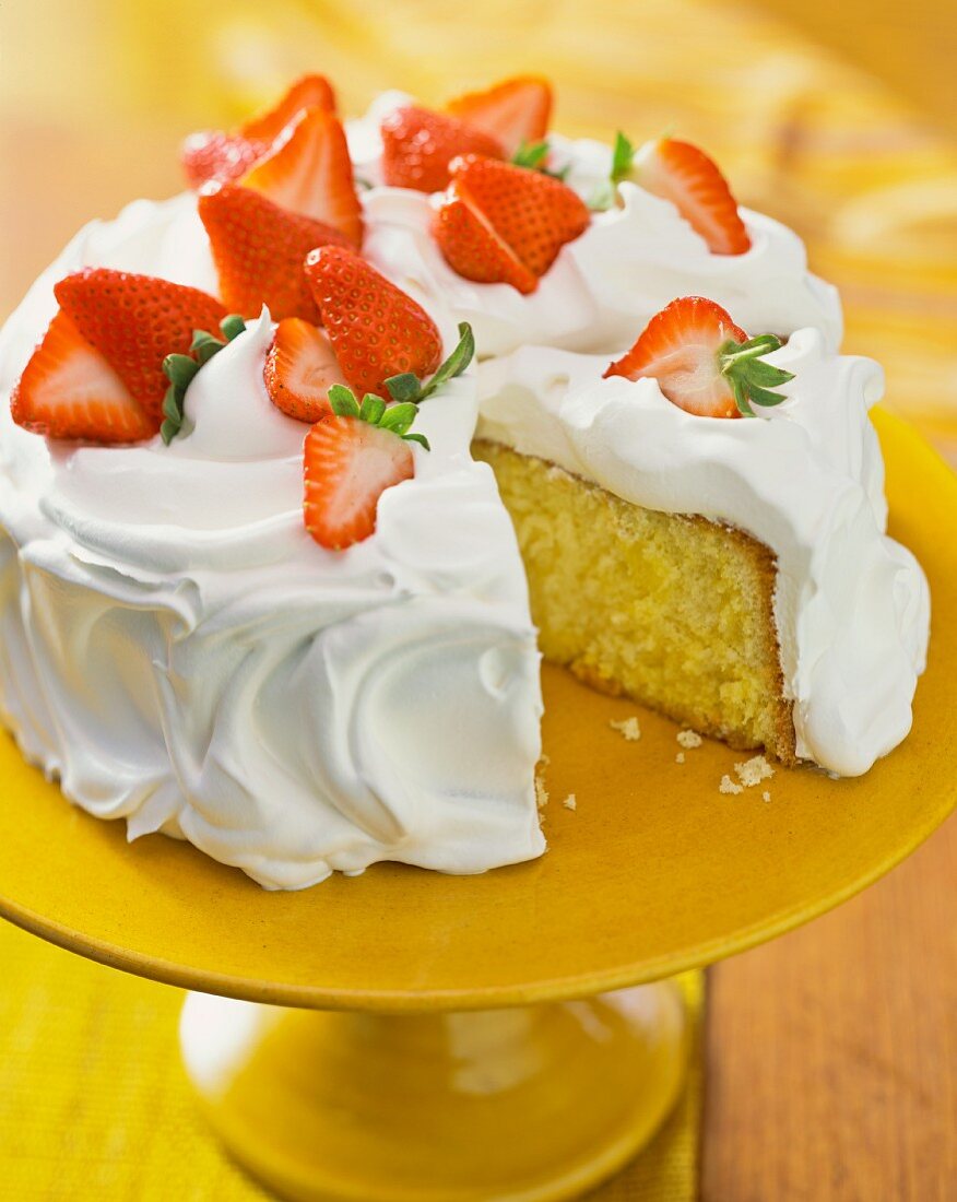 Sponge cake topped with meringue and strawberries, sliced