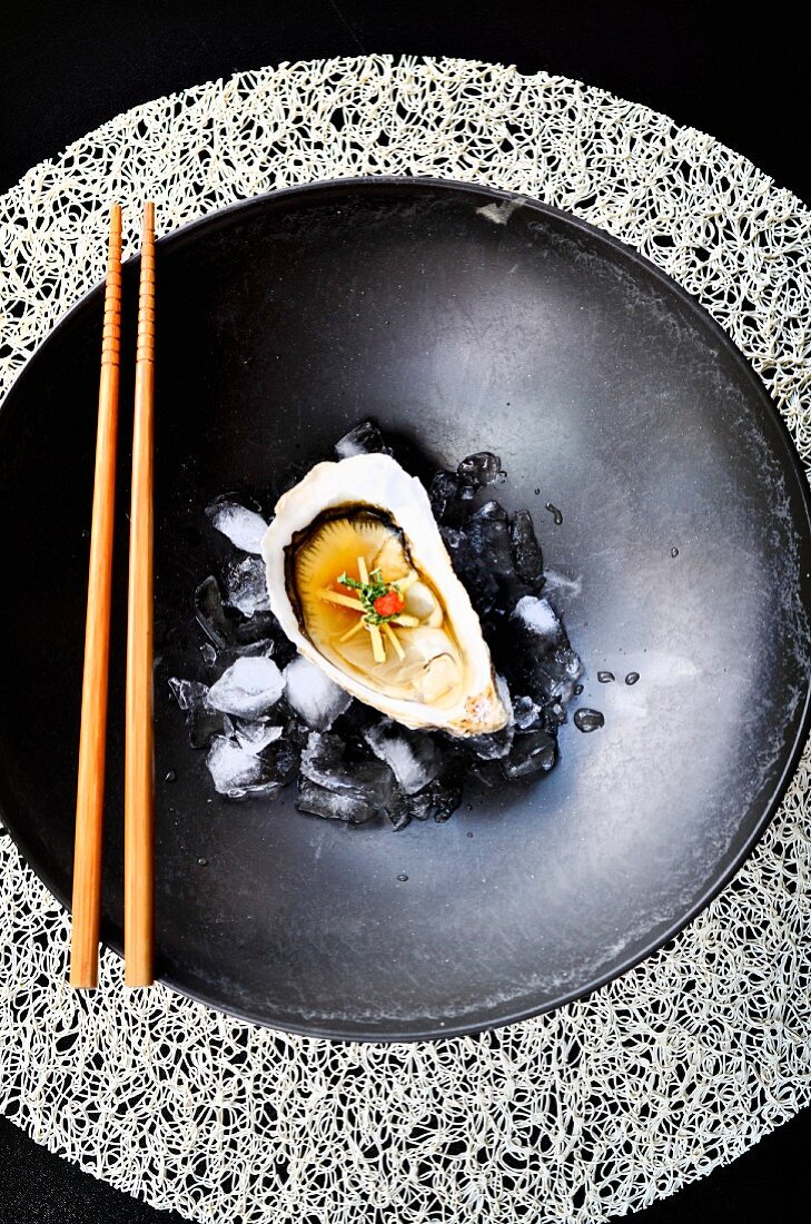 Auster mit Ingwer, Miso und Chili auf Eiswürfeln in schwarzer Schale mit Stäbchen (Japan)