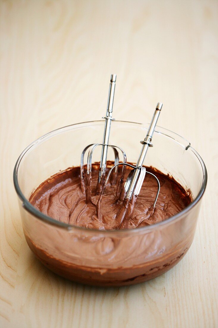 Chocolate cake mix in a glass bowl with whisks