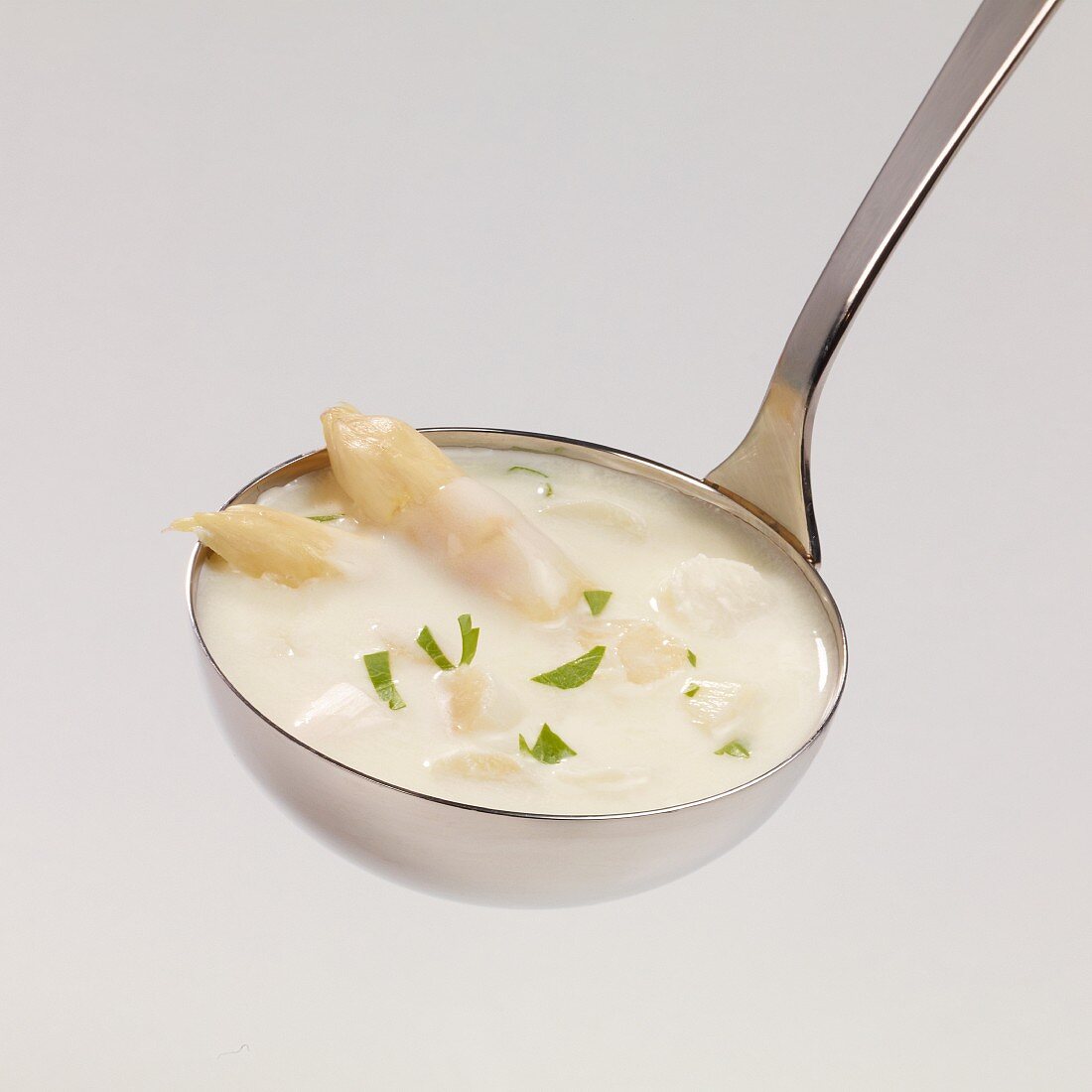 Cream of asparagus soup with chopped parsley in a ladle