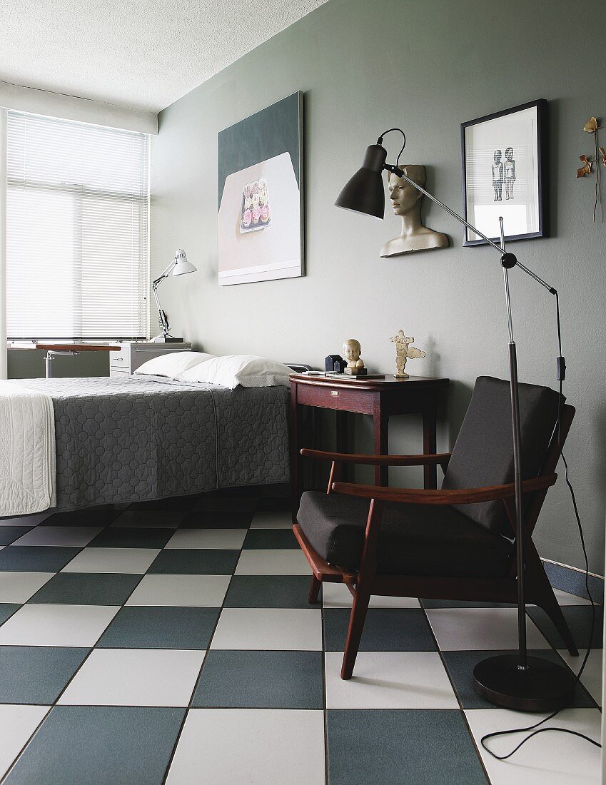 Retro standard lamp next to fifties-style armchair with black upholstery on chequered floor in bedroom painted grey