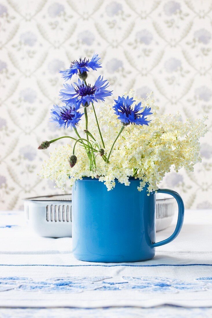 Elderflowers and cornflowers in small, blue enamel pot