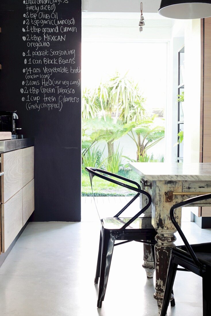 Detail of dining area with metal, retro chairs at shabby-chic table; open door with view of palm trees in courtyard in background