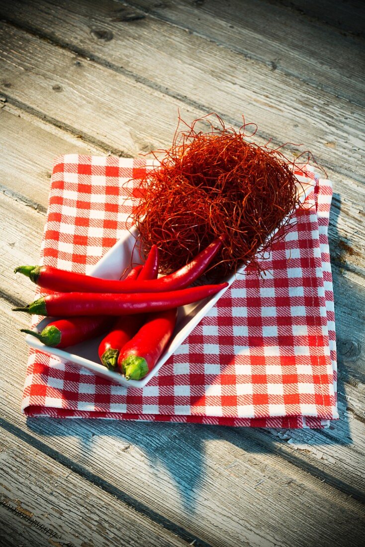 Rote Chilischoten und Chilifäden in einer Schale auf Küchentuch am Holztisch