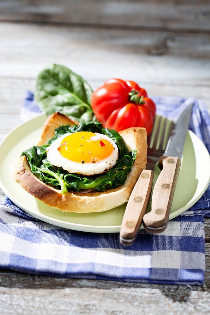 A fried egg and spinach on toast with a beefsteak tomato