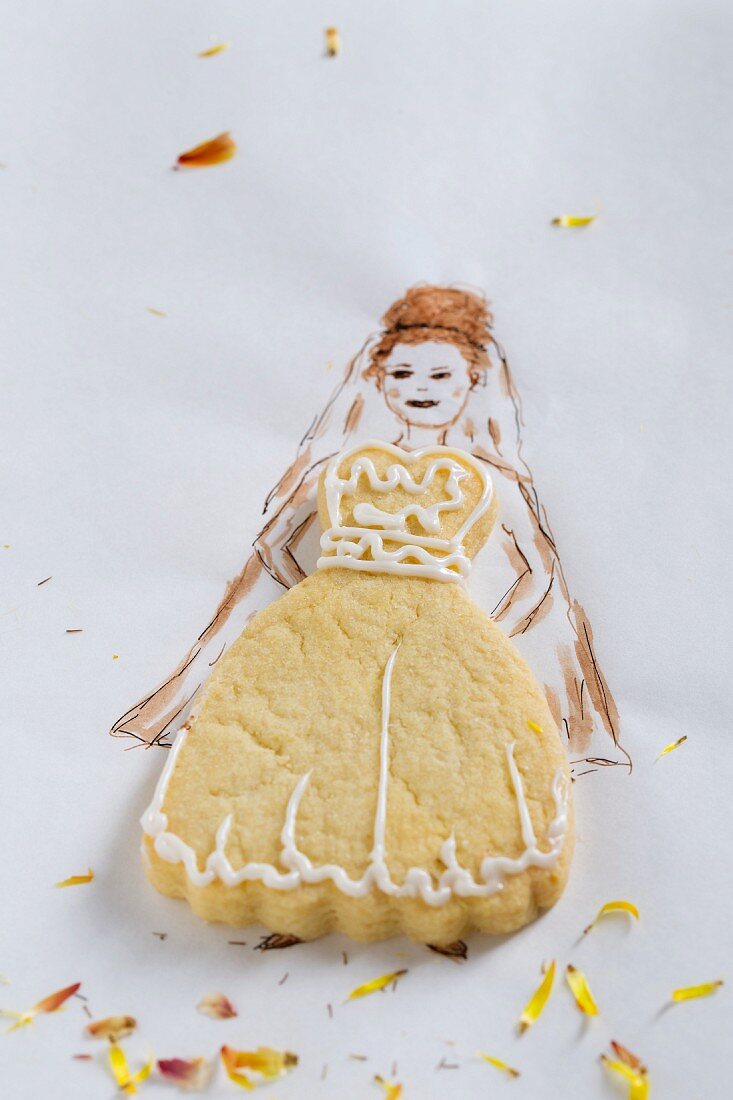 A wedding dress-shaped biscuit on a piece of paper with the bride drawn on