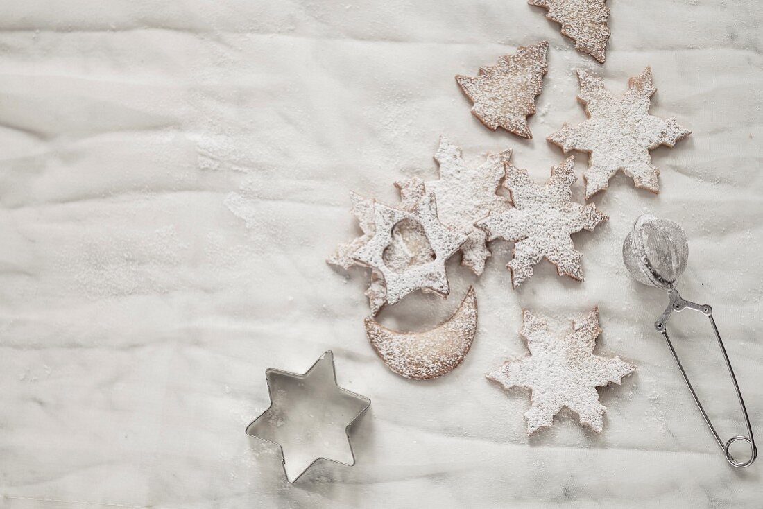 Christmas biscuits dusted with icing sugar with a tea strainer and biscuit cutters