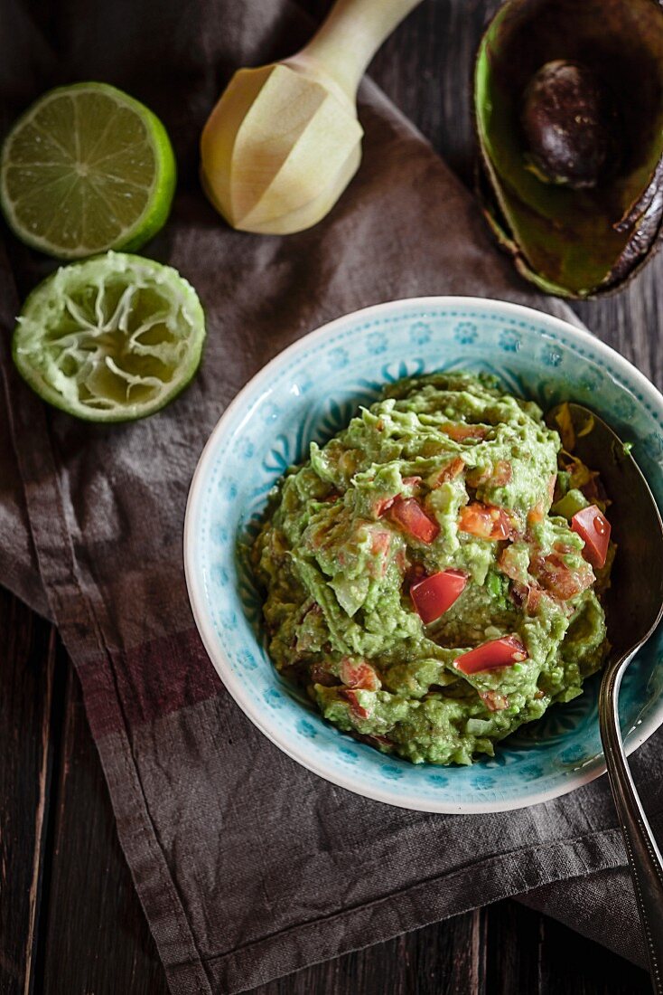 A bowl of guacamole, a hollowed out avocado and a pressed lime half