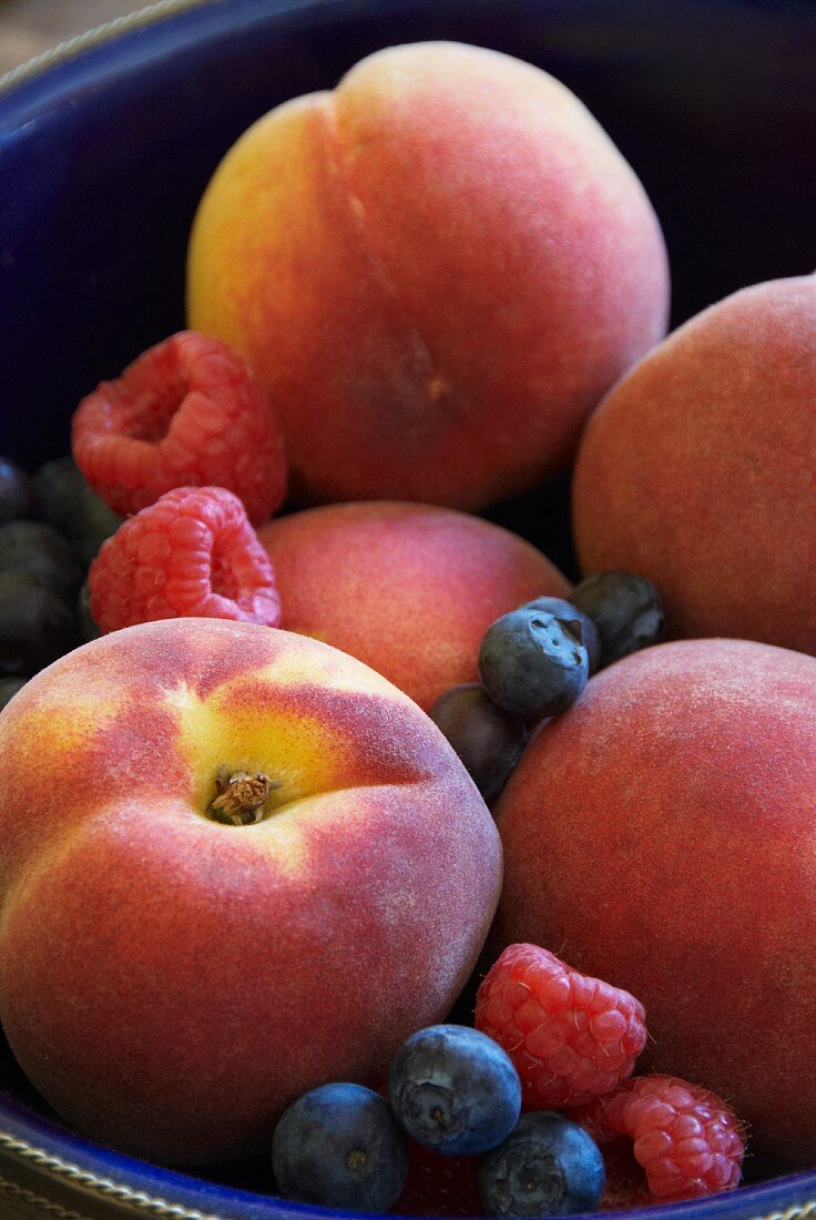 Pfirsiche, Himbeeren und Heidelbeeren in einer blauen Schale