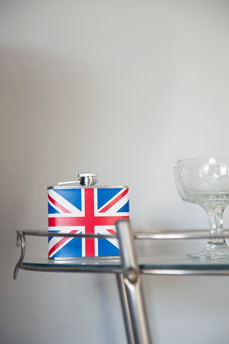 Flachmann mit Unionjack-Motiv und Cocktailgläser auf Glas-Beistelltisch